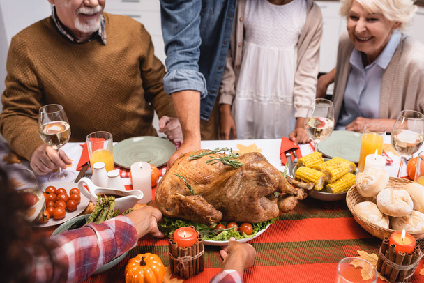 Selective focus of african american woman putting turkey on table near family and thanksgiving dinner  - 写真・画像