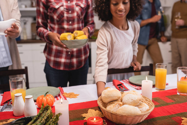 Selective focus of african american girl holding basket with buns near parents during thanksgiving dinner  - Photo, Image