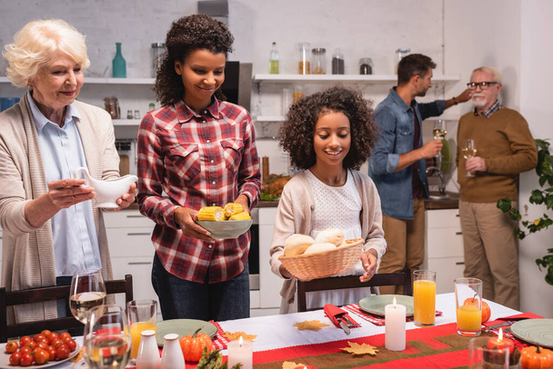 Enfoque selectivo del niño afroamericano sosteniendo bollos cerca de los padres durante la cena de acción de gracias en casa  - Foto, Imagen