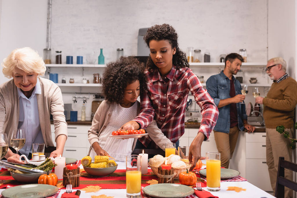 Selective focus of multiethnic women putting food on table near african american girl during thanksgiving  - Фото, изображение