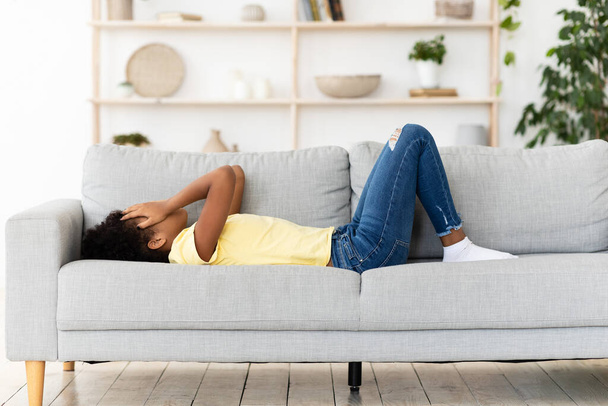 sfrustrowana czarna dziewczyna płacze zakrywając twarz leżąc na kanapie w domu - Zdjęcie, obraz