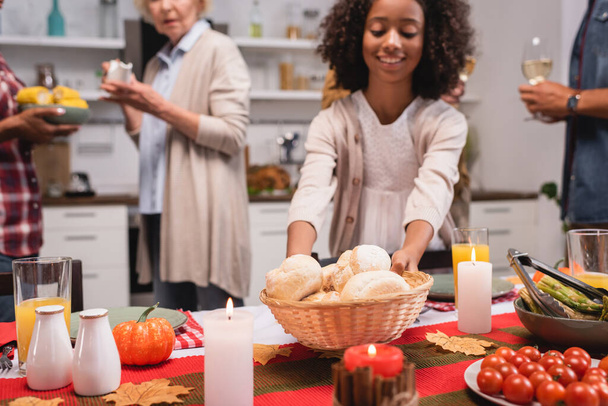 Selective focus of african american kid holding basket with buns near parents during thanksgiving dinner  - Photo, Image