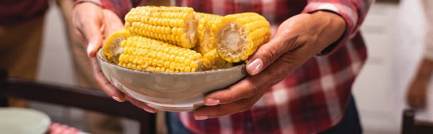 Panoramic crop of african american woman holding bowl of corn at home  - Photo, Image