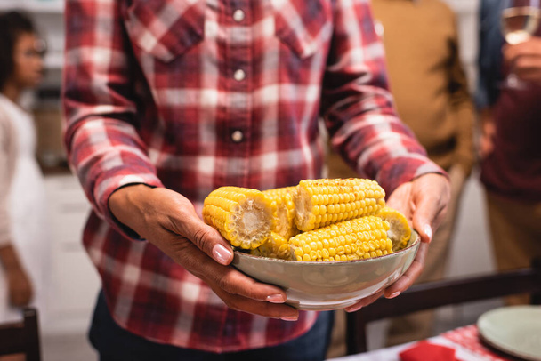 Selective focus of african american woman holding bowl of corn near family during thanksgiving  - Fotó, kép