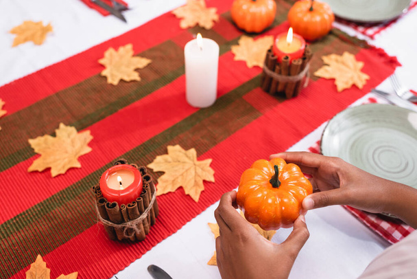 Vista recortada de un niño afroamericano sosteniendo calabaza decorativa cerca de velas en la mesa durante el día de acción de gracias  - Foto, Imagen