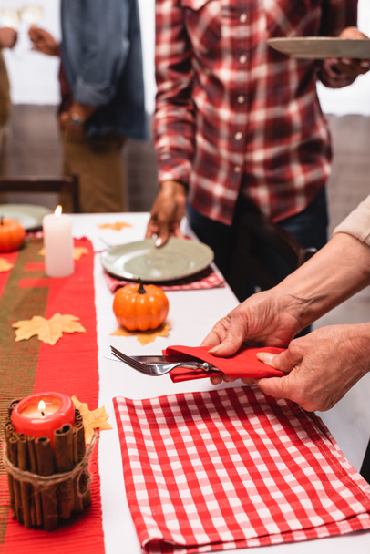 Cropped view of senior woman holding cutlery near table during thanksgiving celebration with multiethnic family  - Foto, Imagen