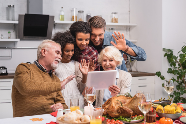Wybiórcze skupienie wielokulturowej rodziny machającej na tablecie cyfrowym podczas wideokonferencji i uroczystości dziękczynienia  - Zdjęcie, obraz
