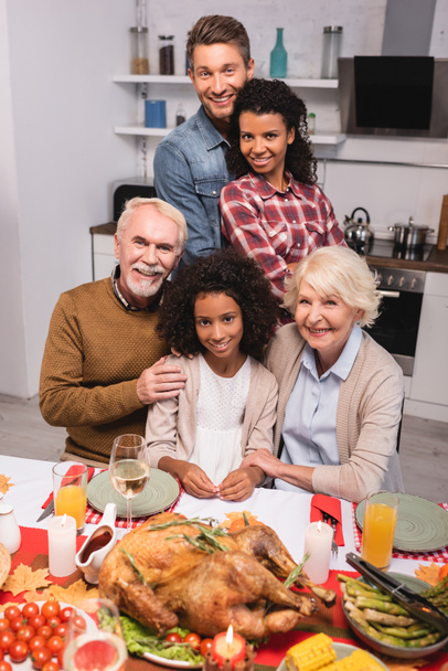 Selective focus of multicultural family hugging near turkey on table during thanksgiving  - Photo, Image
