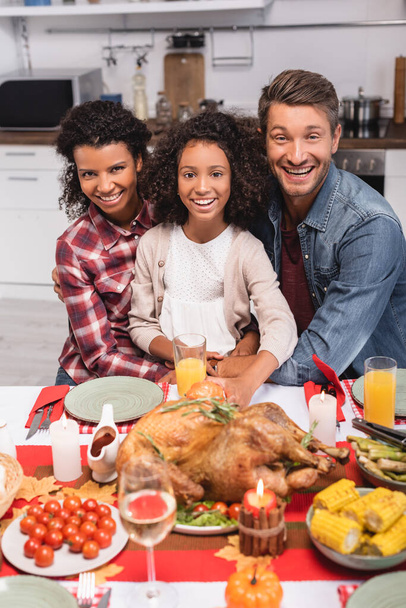 Focus selettivo dei genitori multietnici che abbracciano il bambino africano americano vicino al cibo durante il Ringraziamento  - Foto, immagini