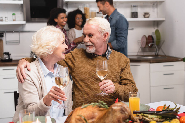 Selective focus of senior man embracing wife during celebration of thanksgiving with multiethnic family  - Photo, Image