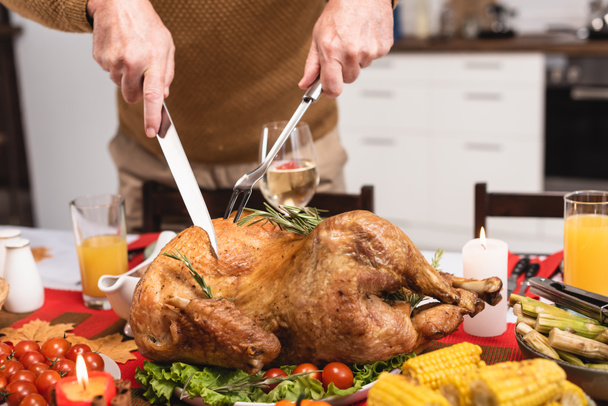 Cropped view of senior man cutting turkey near candles during thanksgiving dinner  - Photo, Image