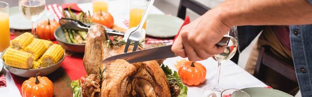 Horizontal crop of man cutting turkey near decorations during thanksgiving dinner  - 写真・画像