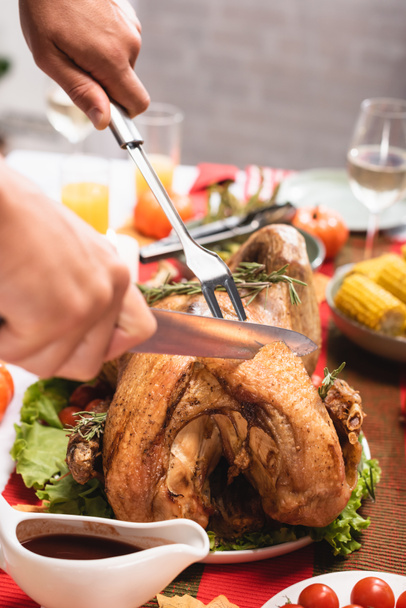 Vista ritagliata dell'uomo che taglia il tacchino vicino al cibo durante la celebrazione del Ringraziamento  - Foto, immagini