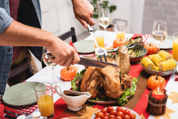 Cropped view of man cutting turkey near thanksgiving decorations on table  - Фото, зображення