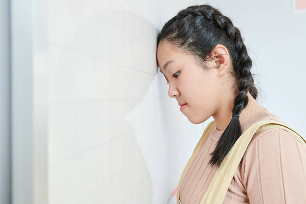 Gestresstes und müdes asiatisches Teenager-Mädchen lehnt aufgebracht an Wand, nachdem es die Prüfung nicht bestanden hat - Foto, Bild