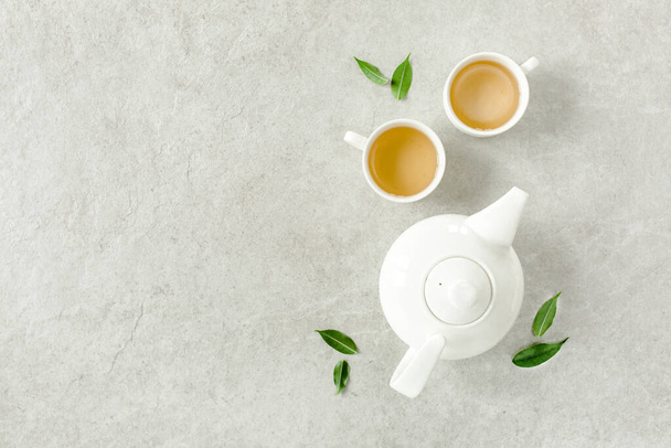 Herbal tea with two white tea cups and teapot, with green tea leaves. Flat lay, top view. Tea concept - Фото, изображение