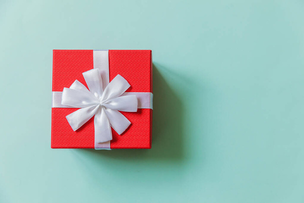Noel yeni yıl sevgililer günü kutlaması. Romantik bir hediye. Pastel mavi renkli arka planda izole edilmiş en az tasarım kırmızı hediye kutusu. Düz görünüm kopyalama alanı - Fotoğraf, Görsel