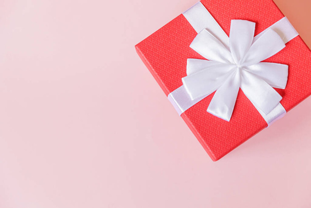 Kerstmis Nieuwjaar verjaardag Valentijnsdag presenteren romantisch concept. Eenvoudig minimale ontwerp rode geschenkdoos geïsoleerd op pastel roze kleurrijke achtergrond. Flat lay bovenaanzicht kopieerruimte - Foto, afbeelding