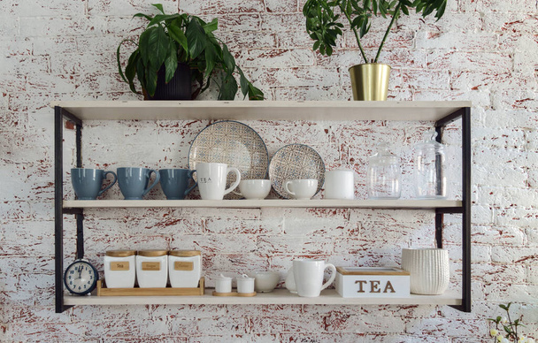 Γυάλινα σκεύη κουζίνας Κύπελλα και δίσκοι σε ξύλινα και μεταλλικά ράφια κουζίνας σε bick τοίχο - Φωτογραφία, εικόνα