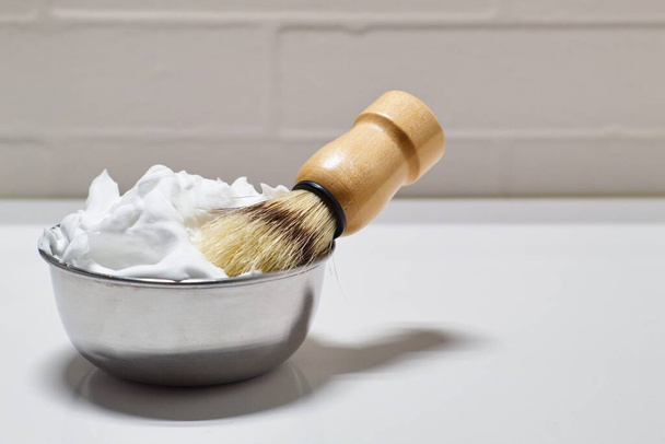 Bol avec mousse à raser et brosse sur fond blanc dans la salle de bain - Photo, image
