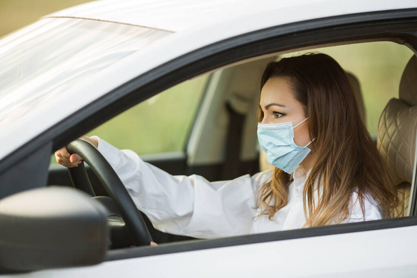 beautiful young woman in medical mask driving a car - Foto, Bild