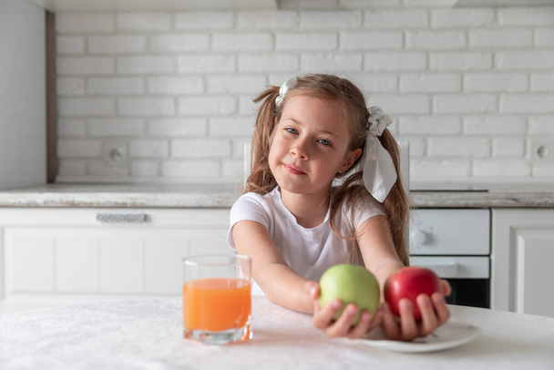 little girl with juice and fruit apples in the kitchen. healthy food. vegetarianism. vitamins. Copy space - Fotografie, Obrázek