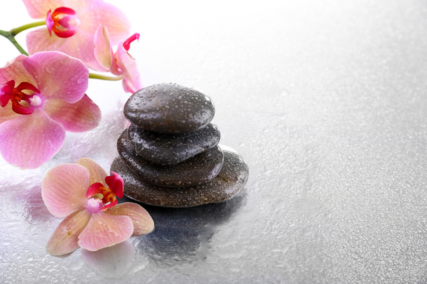 Composition with beautiful blooming orchid with water drops and spa stones, on light background - Fotó, kép
