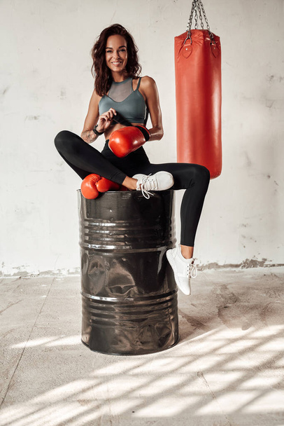 Slim woman with gloves sitting on barrel with bag behind - Photo, image