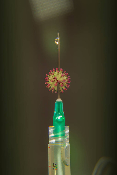 détail de l'aiguille de seringue sur fond noir avec une goutte de médicament et le symbole du coronavirus - Photo, image