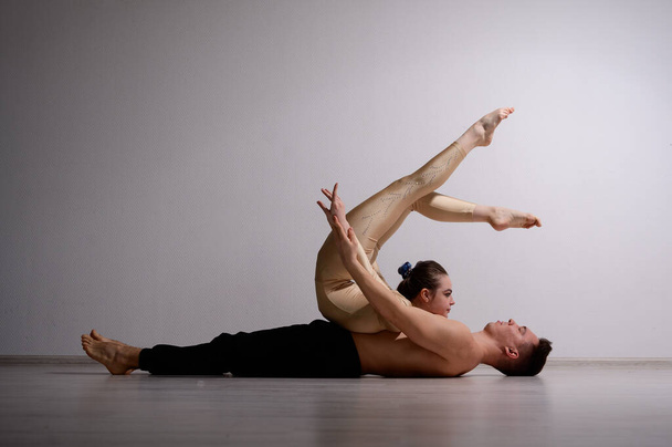 A duet of acrobats showing a pair trick. A woman in gymnastics overalls in a handstand over a shirtless man lies on his back. Very flexible circus performers. - Foto, Bild
