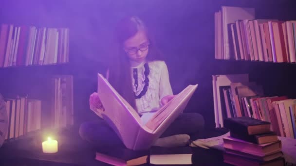 Egy lány nyit egy mesekönyvet a könyvtárban, színes füst kavarog körülötte, gyertyákat gyújtanak a közelben. - Felvétel, videó
