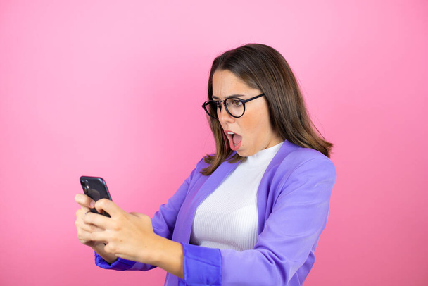 Giovane bella donna d'affari su isolato sfondo rosa chatta con il suo telefono e sorpreso - Foto, immagini