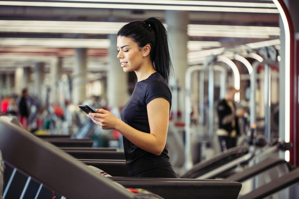 young Sportswoman using smartphone while jogging on treadmill - Photo, Image