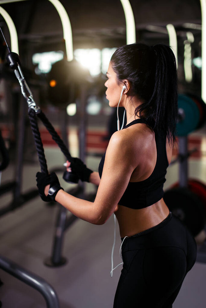 rear view fit woman execute exercise with exercise-machine Cable Crossover in gym - Photo, image