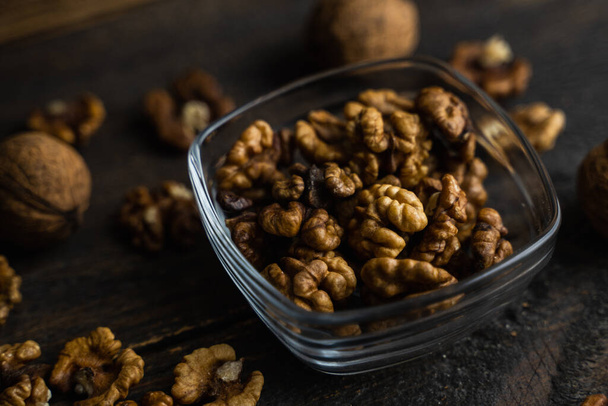 Walnut in a smale plate with scattered shelled nuts and whole nut which standing on a wooden vintage table. Walnuts is a healthy vegetarian protein nutritious food. Walnut on rustic old wood. - Foto, Imagem