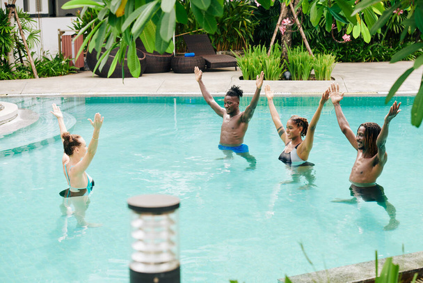 Jovens animados multi-étnicos que se repetem após o treinador de aeróbica aquática ao se exercitar na piscina - Foto, Imagem