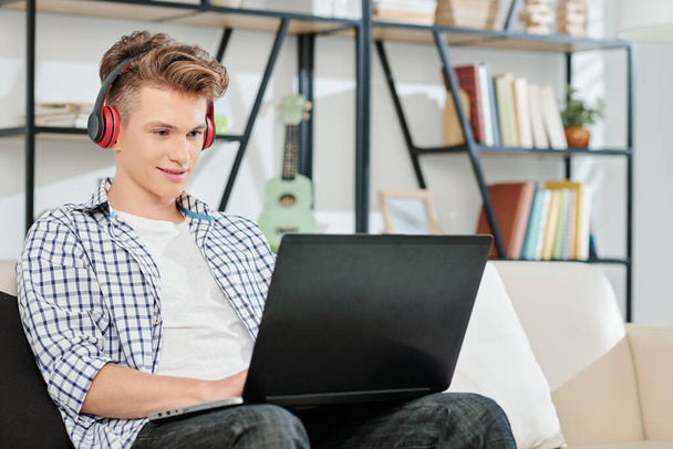 Nastolatek słuchający muzyki w słuchawkach podczas pracy lub gry na laptopie - Zdjęcie, obraz