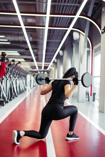 girl doing lunges with barbell in modern gym - Foto, Imagen