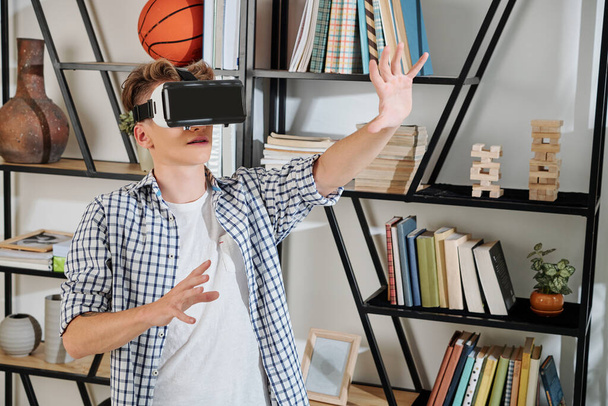 Teenager standing at bookshelf and testing new virtual reality application - Foto, afbeelding