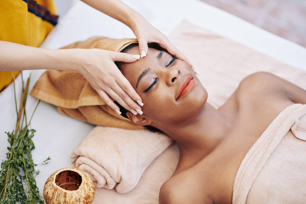 Sorridente giovane donna ottenere rilassante massaggio viso ringiovanente nel salone spa, vista dall'alto - Foto, immagini