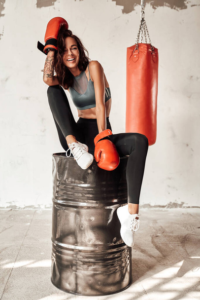 Slim woman with gloves sitting on barrel with bag behind - Foto, Imagen