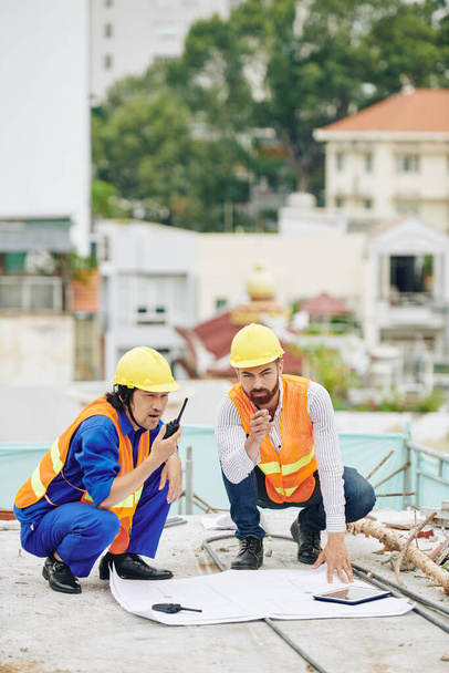 Head engineer checking construction plan when contractor controlling work of builders via walkie-talkie - Foto, Bild