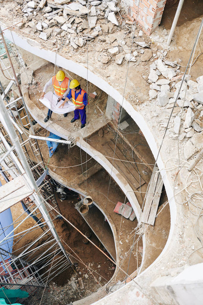 Οικοδόμος δείχνει το σχέδιο κατασκευής στον εργολάβο όταν συζητούν κάτοψη, θέα από ψηλά - Φωτογραφία, εικόνα