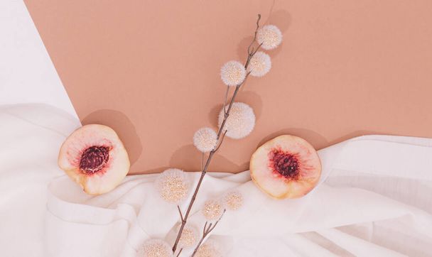 Still life scene with fresh peach and decor flowers on white textile background. Minimal aesthetic. - Foto, afbeelding