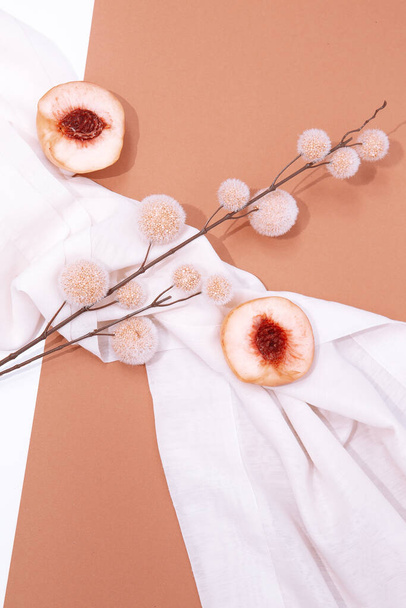 Still life scene with fresh peach and decor flowers on white textile background. Minimal mood aesthetic. - Photo, image