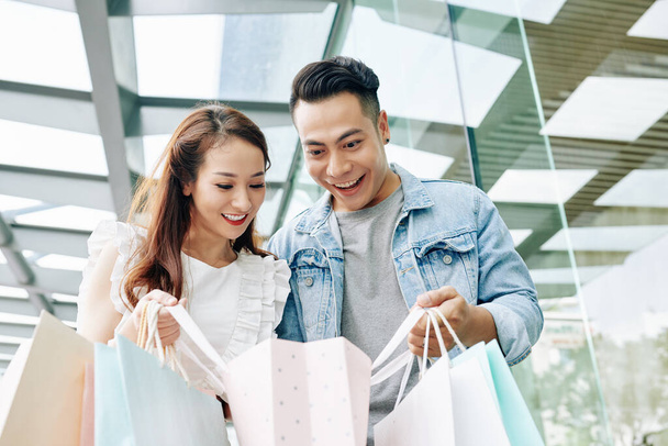 Excited young Vietnamese couple looking in paper bag after shopping in mall - Photo, Image
