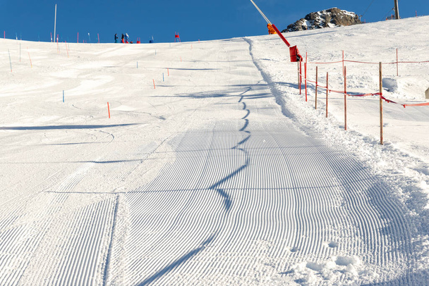 Filas de línea recta de pista de esquí recién preparada con sol brillante y fondo azul claro. Montaña nevada paisaje cuesta abajo en la estación de esquí de invierno de Europa. - Foto, imagen