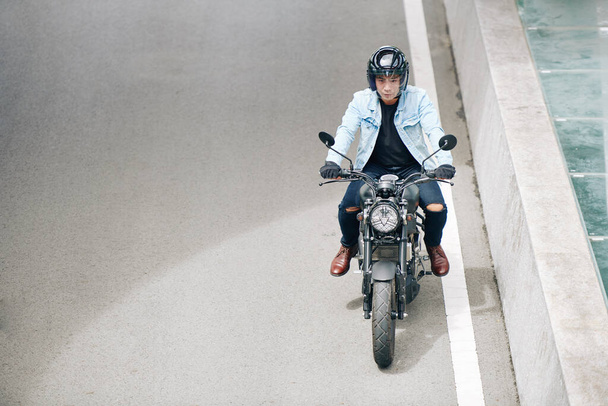 Серйозний мотоцикліст їде швидко по шосе, він весело їздить по порожній дорозі
 - Фото, зображення
