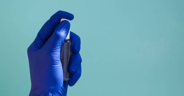 A hand in a rubber medical glove sprays anaesthetic on a green background. - Photo, Image