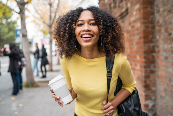 Portrait of young afro american woman laughing and holding a cup of coffe in the street. Outdoors. - Foto, Imagen